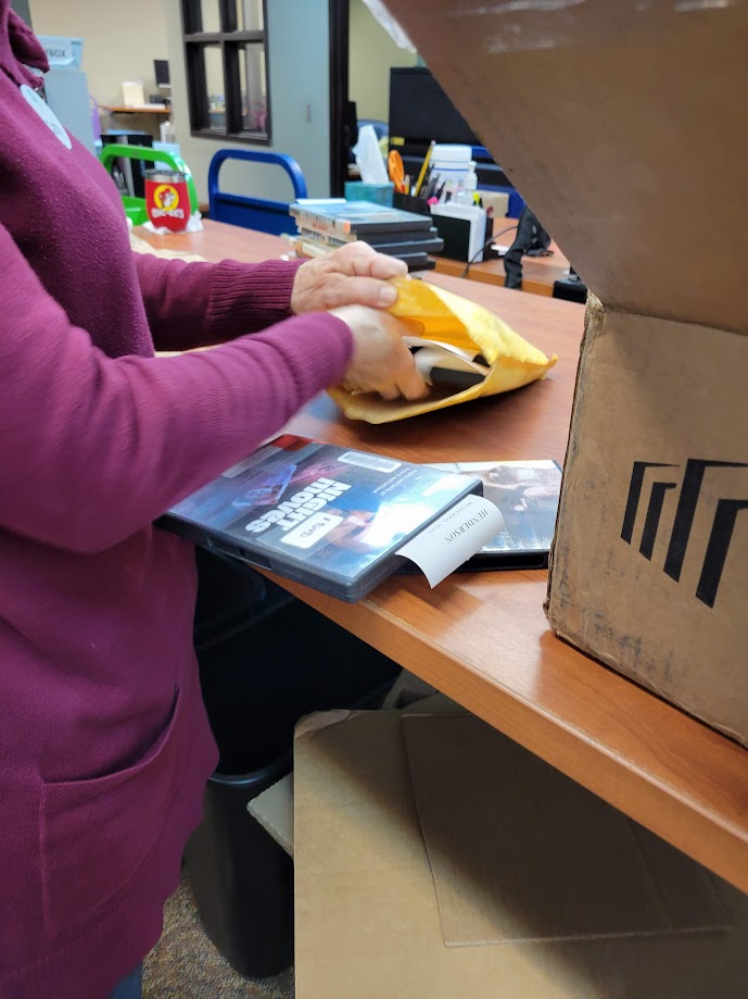 A staff member placing DVDs inside of a padded envelope.