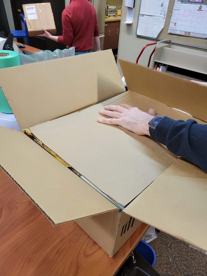 A staff member placing a sheet of cardboard on top of the materials in a cardboard box.