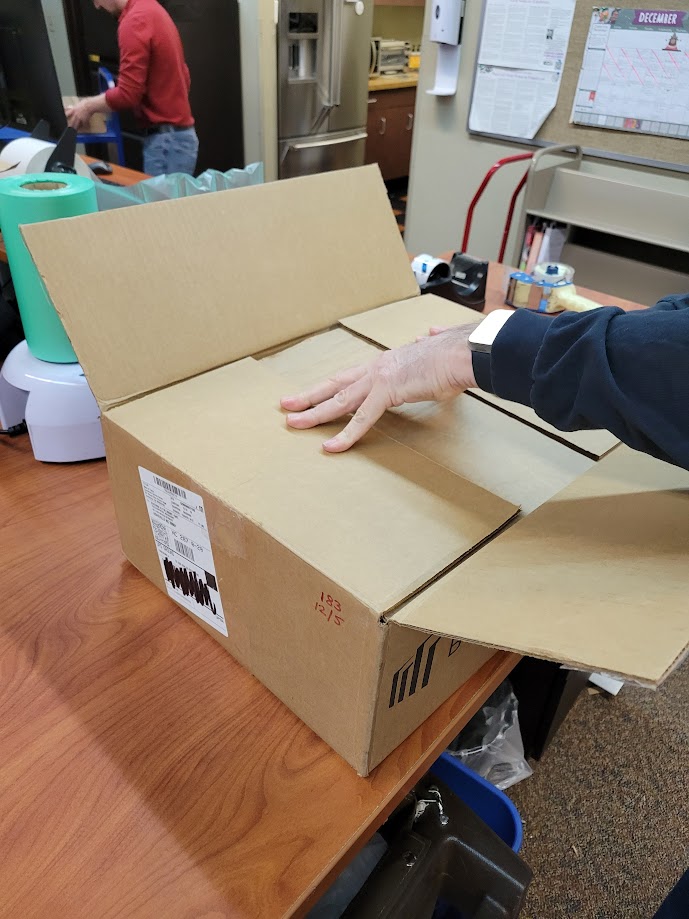 A staff member folding down the flaps of a cardboard box.